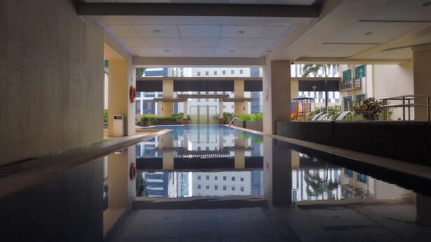 Een modern binnenzwembad met heldere reflecties op het water, omringd door een lage muur en een balkon met planten.