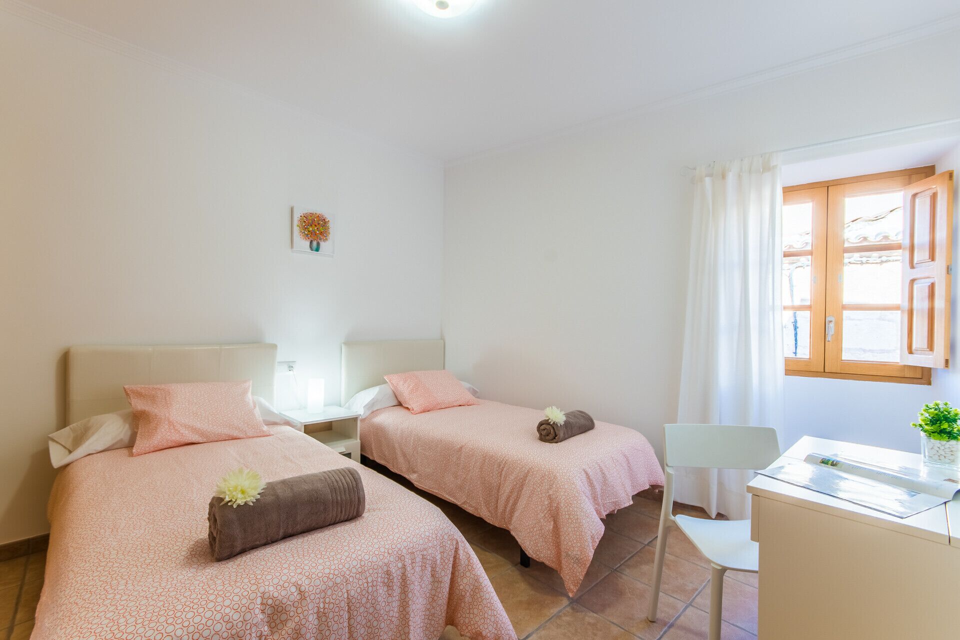 A two-bed room with matching pink bedding, a small desk, and a window with curtains.