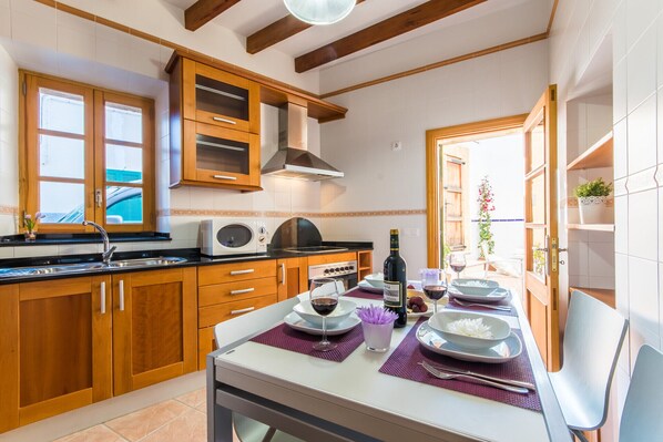 A modern kitchen with wooden cabinets, a built-in microwave, and a dining area set for a meal. - Holiday home Barbera in Alcudia Old Town (Alcúdia)