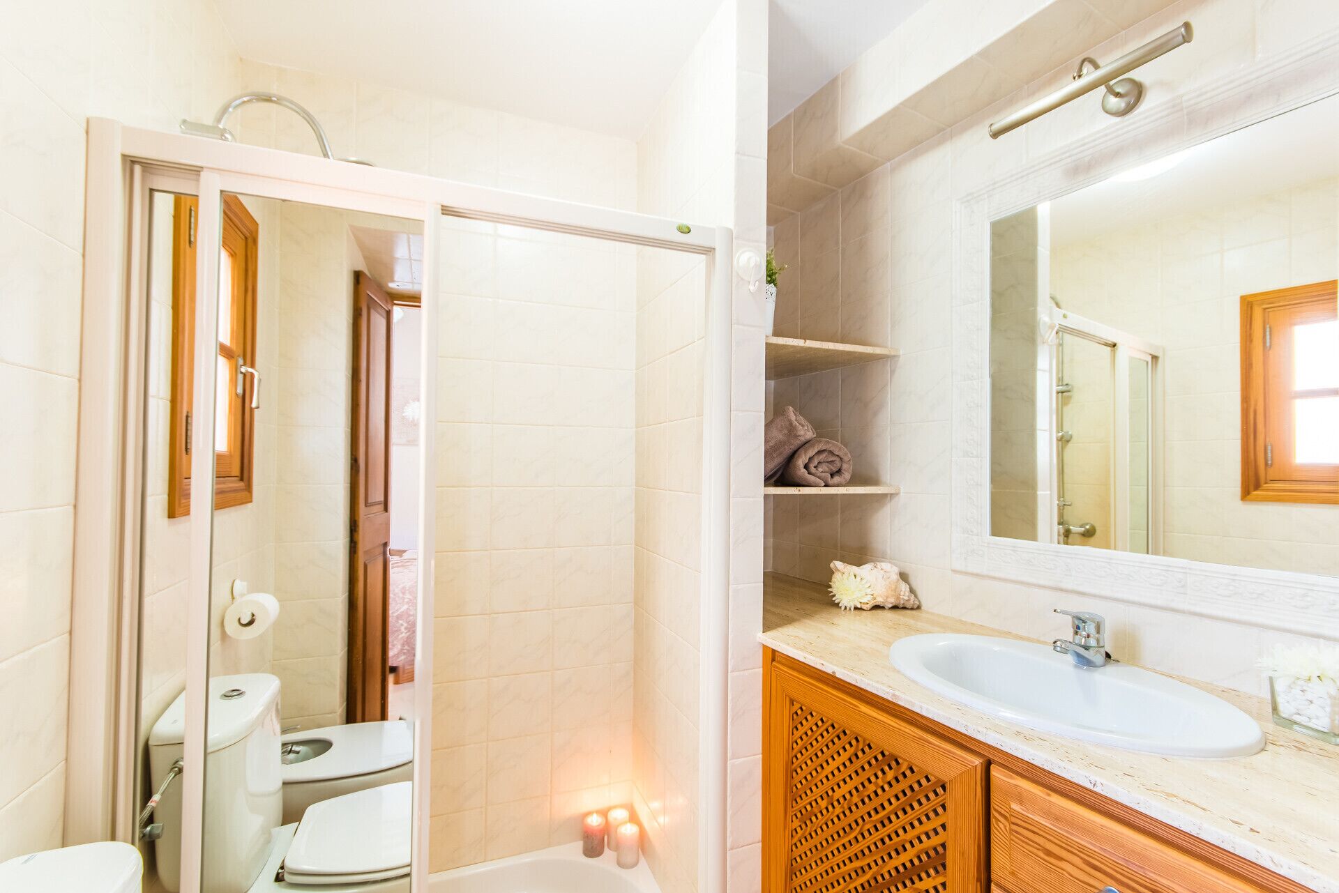 A bathroom with a toilet, sink, and bathtub. There is a mirror above the sink and a shelf with towels.