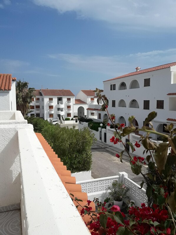 Un bâtiment blanc avec des toits recouverts de tuiles rouges, un escalier et une vue sur une cour intérieure agrémentée de plantes et de fleurs en pot.