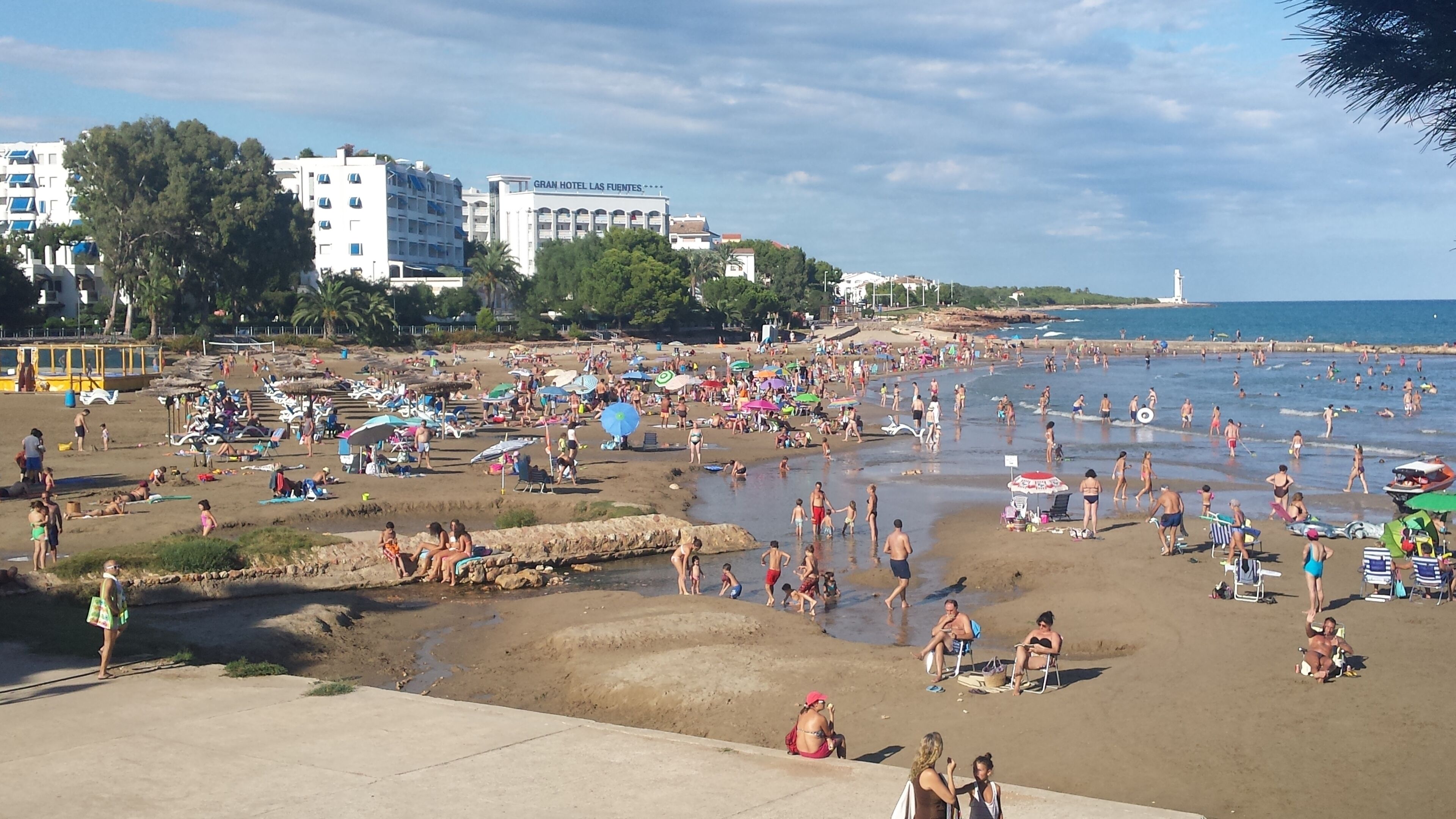 A crowded beach with people sunbathing and swimming. There are umbrellas and beach chairs.