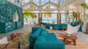 A spacious indoor area with teal sofas, a large window overlooking the beach, and a ceiling fan. -  The Standard, Maldives, by Hyatt (Huruvalhi)