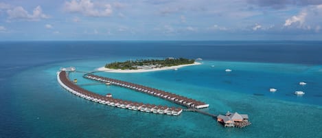 An overwater bungalows connected by a dock, surrounded by turquoise waters and a small island.
