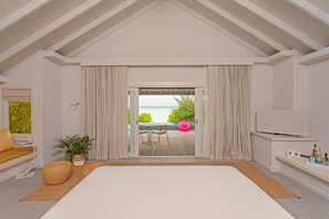 A modern bedroom with a large bed, a view of the sea, and a balcony with outdoor furniture.