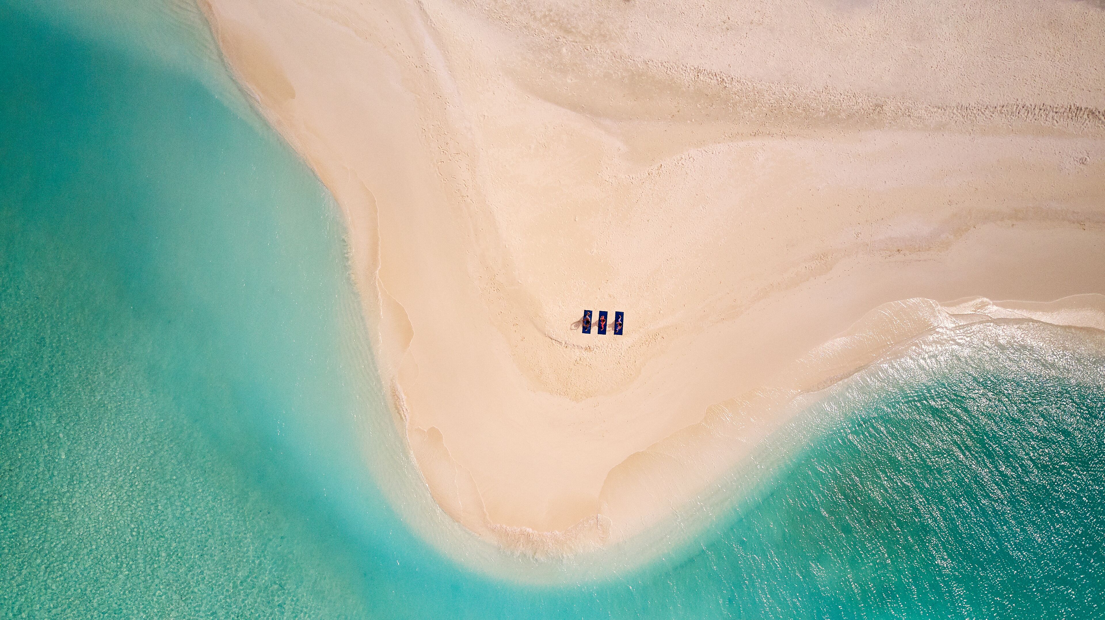 Eine Vogelperspektive zeigt einen Strand mit einer schmalen Sandfläche, die zwei Wassermassen voneinander trennt.