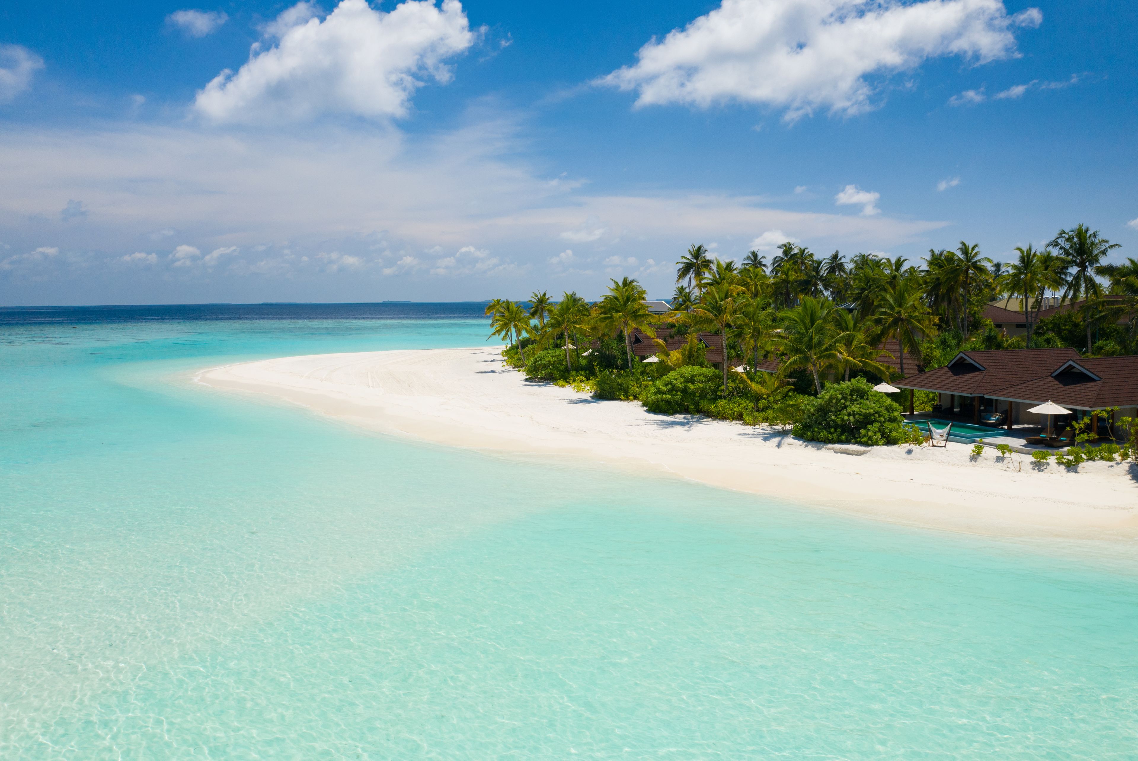 A beach resort with a white sandy shore, clear turquoise waters, and palm trees.