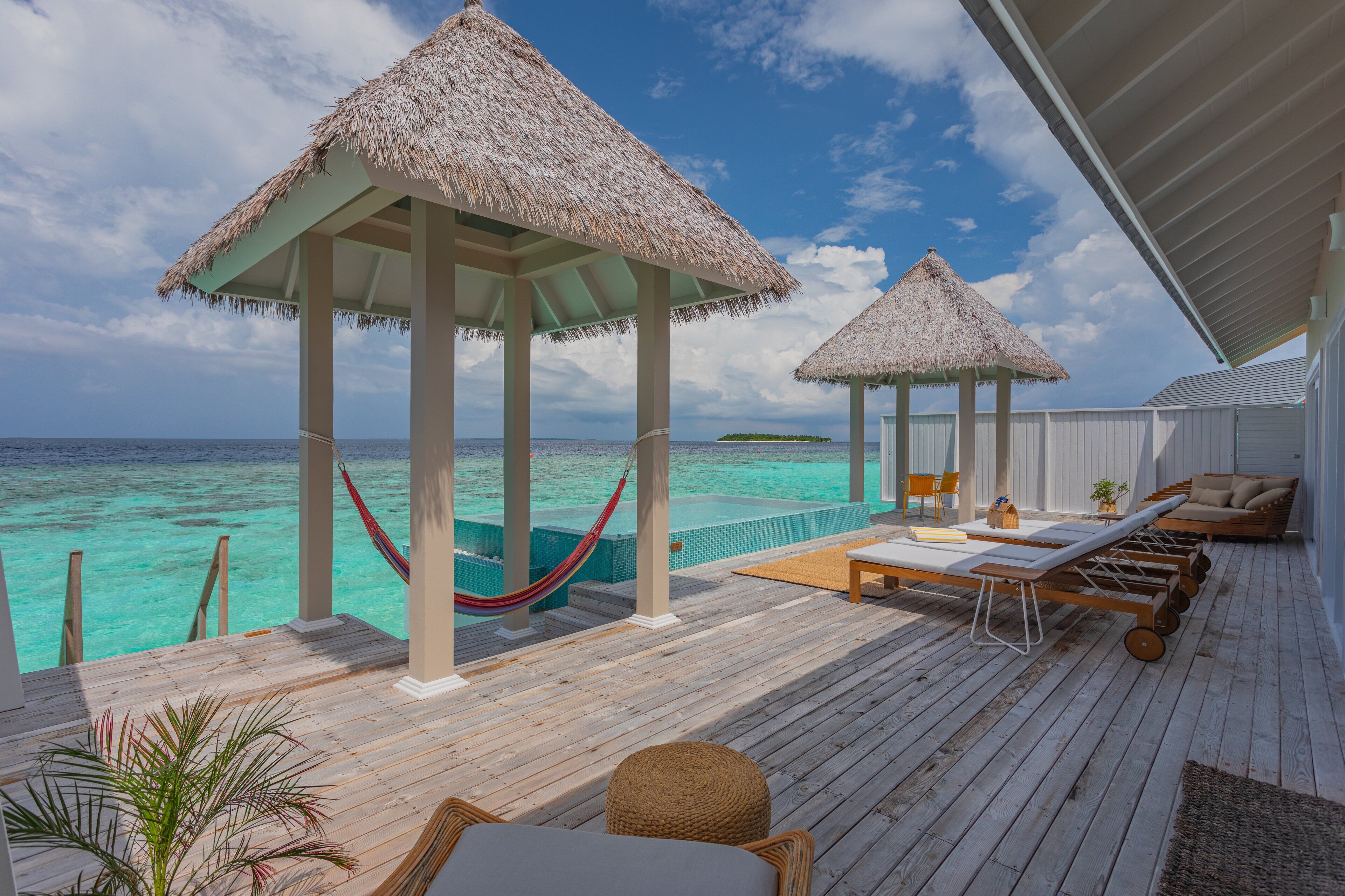Een houten terras met rieten parasols, loungestoelen en een klein zwembad met uitzicht op turquoise water.
