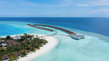 Vista aérea de un resort con un muelle largo que se adentra en aguas turquesas, rodeado de playas de arena blanca y vegetación exuberante.