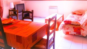 A room with a wooden table and chairs, a sofa, a television, and a window.