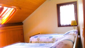 A bedroom with two beds, wooden ceiling beams, a window with a curtain, and a bedside lamp.