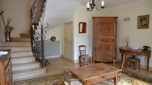 A staircase with ornate metal railings, a wooden table with chairs, a large cabinet, and a chandelier.