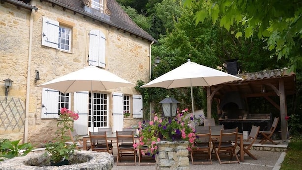 A stone building with a patio area featuring outdoor seating and a barbecue setup.