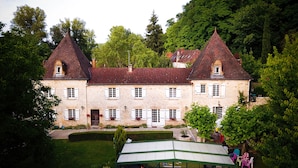 A large stone building with multiple chimneys, a central entrance, and a well-maintained garden.
