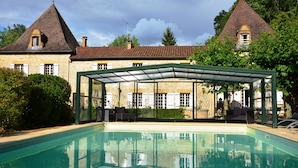 A swimming pool with a glass enclosure, stone buildings, and a clear sky.
