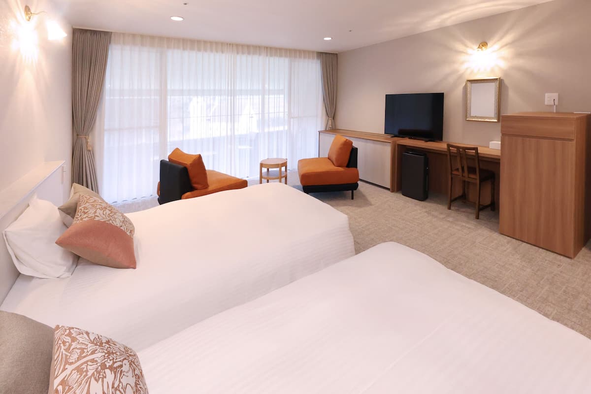 A hotel room with two beds, a desk, a television, and a small refrigerator.