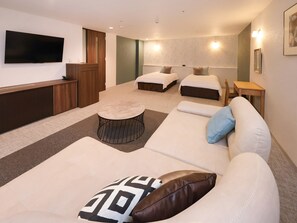 Ein Hotelzimmer mit einer Couch, zwei Betten, einem Fernseher und einem kleinen Tisch.