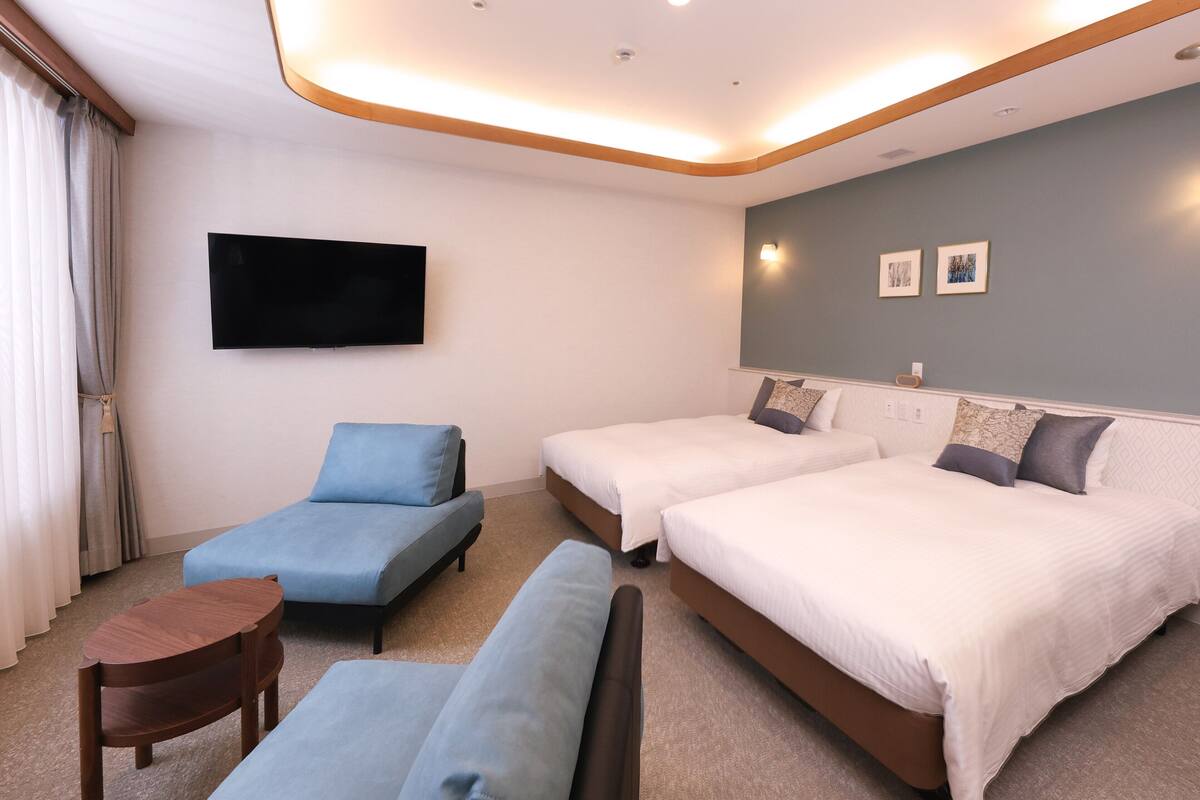 A hotel room with a flat-screen TV, two beds, a sofa, and a small wooden table.