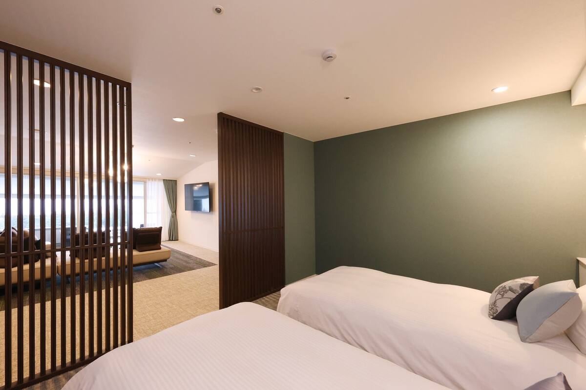 A hotel room with two beds, a sofa, a TV, and a view of the city.