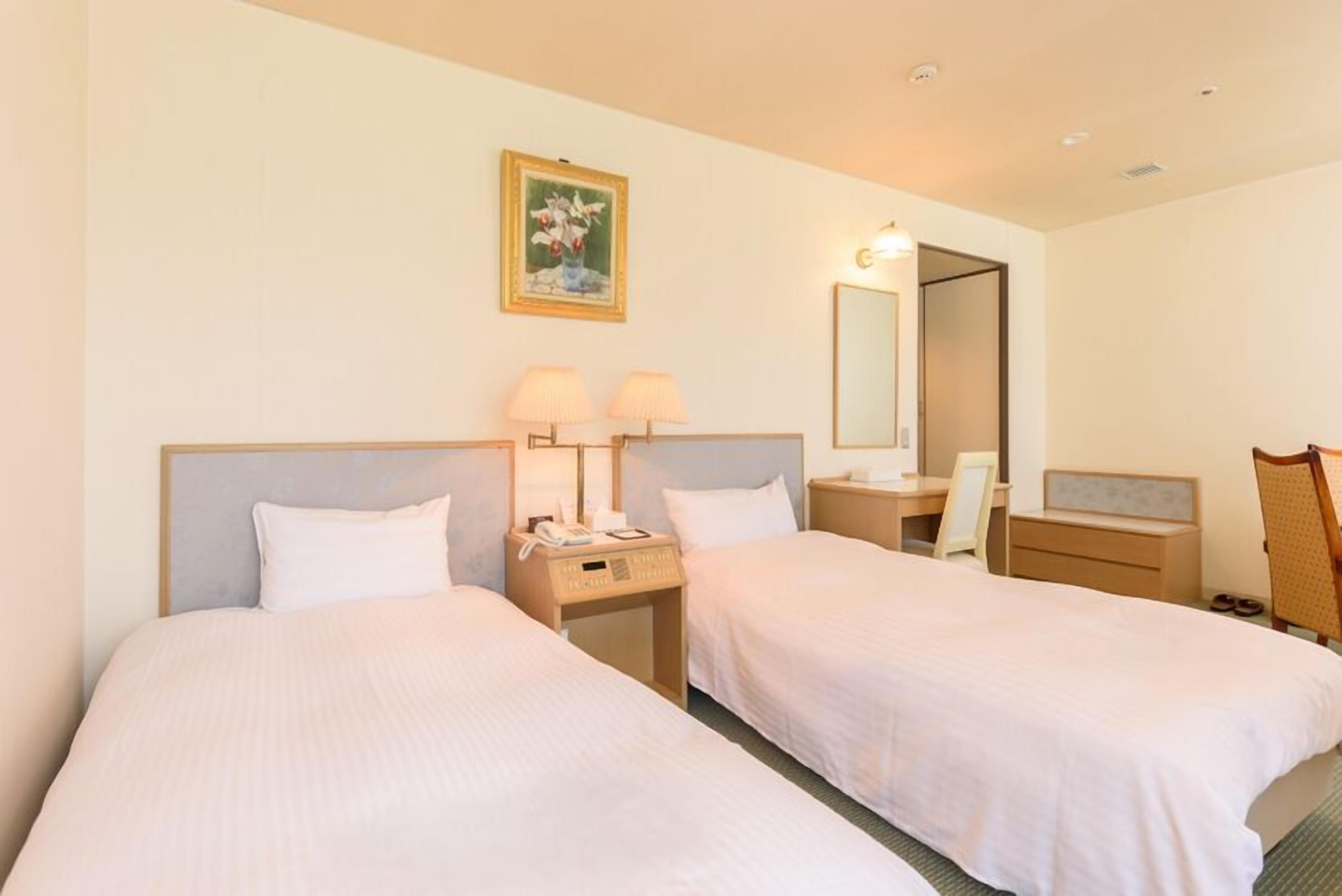 Une chambre d’hôtel avec deux lits, un bureau, une chaise, un miroir et un tableau au mur.