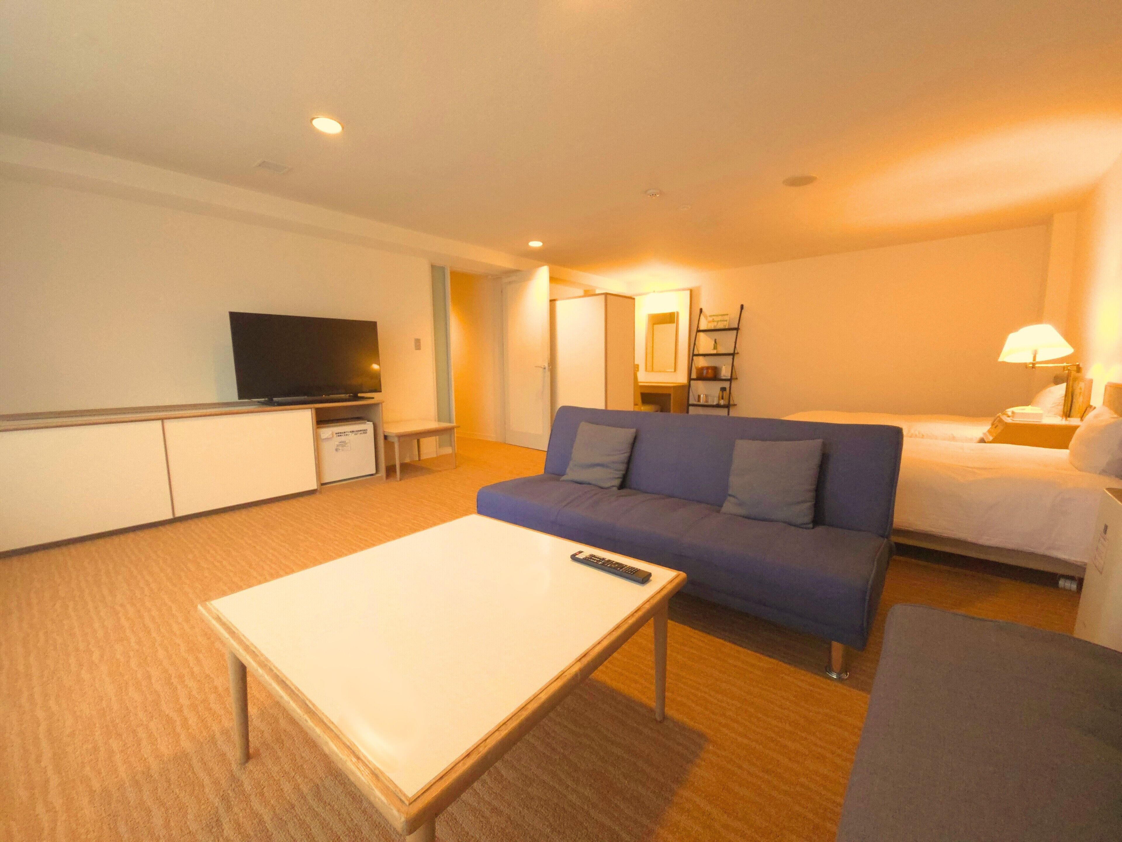 A hotel room with a sofa, a bed, a TV, a desk, and a lamp.