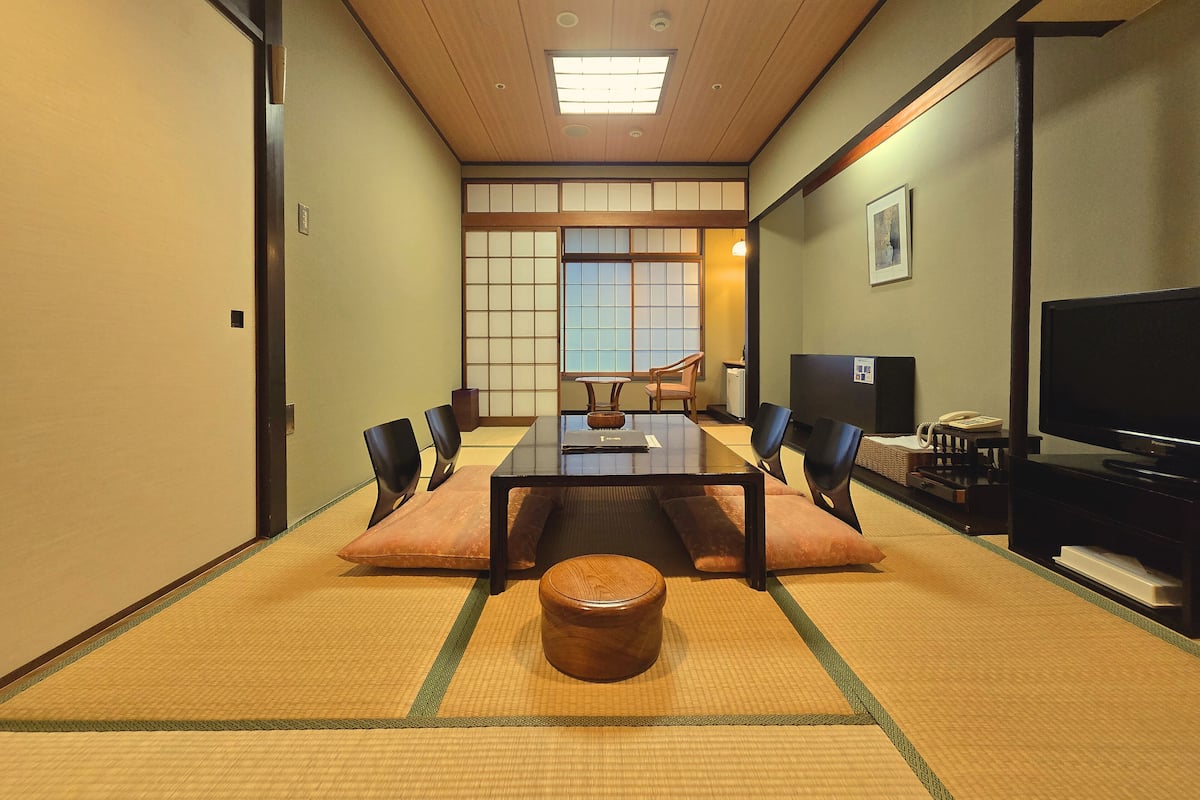 A traditional Japanese-style room with tatami flooring, a low table with cushions, a television, and a sliding door with shoji screens.