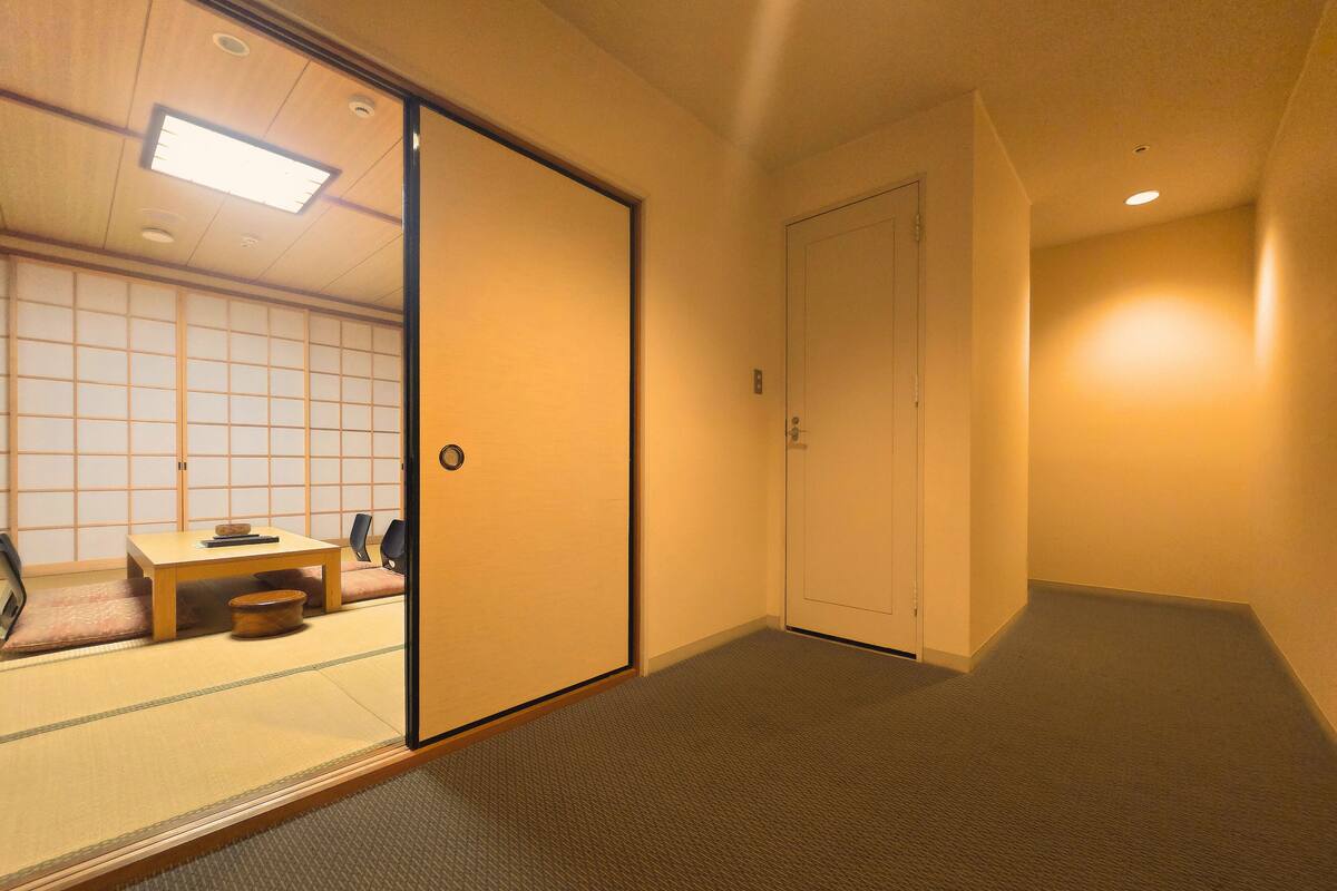 A hotel room with a sliding shoji screen door, a small table with chairs, and a carpeted floor.