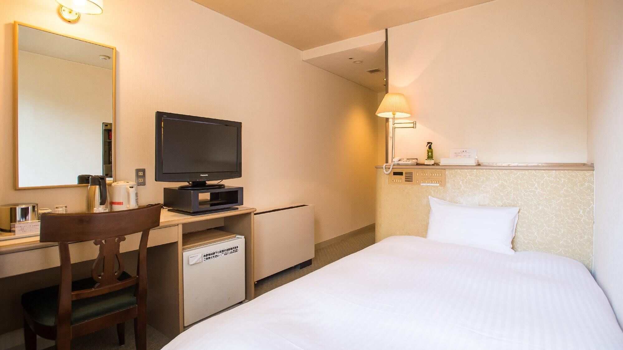Une chambre d’hôtel comprenant un lit, un bureau avec une télévision, une chaise, un miroir, une lampe et un mini-bar.