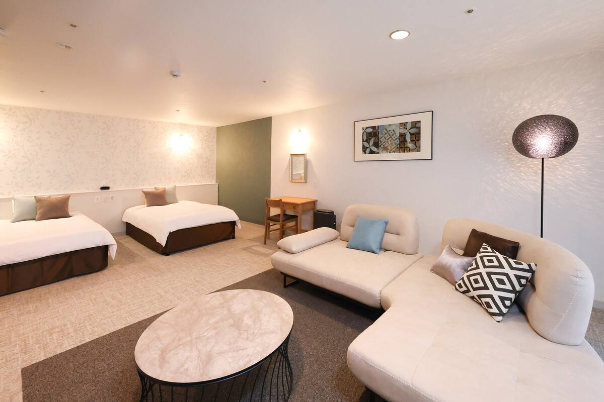 A hotel room with two beds, a sofa, a small table, and a lamp.