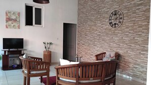 A living room with a TV, wooden chairs, a red rug, a clock, and a wall with a brick pattern. - The Saint-louis River villa Cattleya  (La Rivière Saint-Louis)
