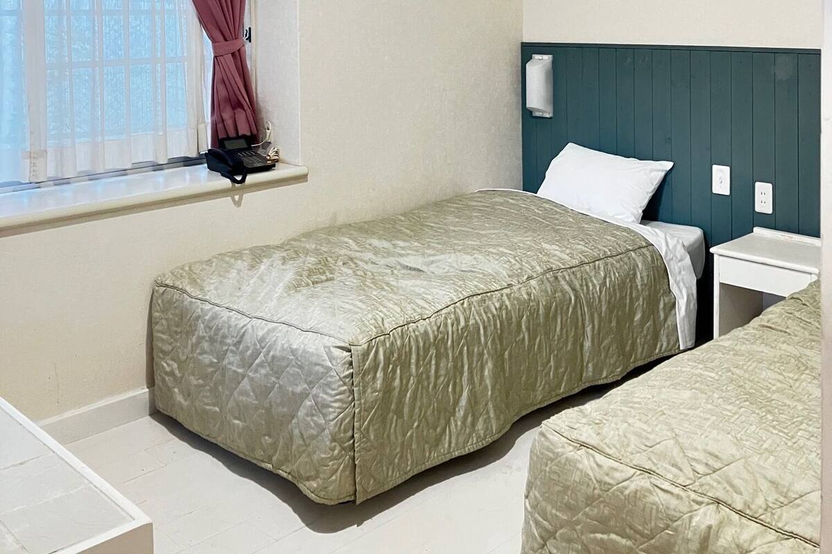 A single-bed room with a window, a bedside table, a nightstand, and a headboard.