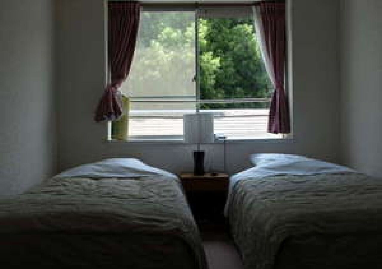 A room with two single beds, a nightstand with a lamp, and a window with curtains.