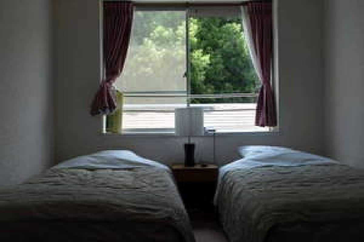 Une chambre avec deux lits simples, une table de chevet avec une lampe et une fenêtre avec des rideaux.