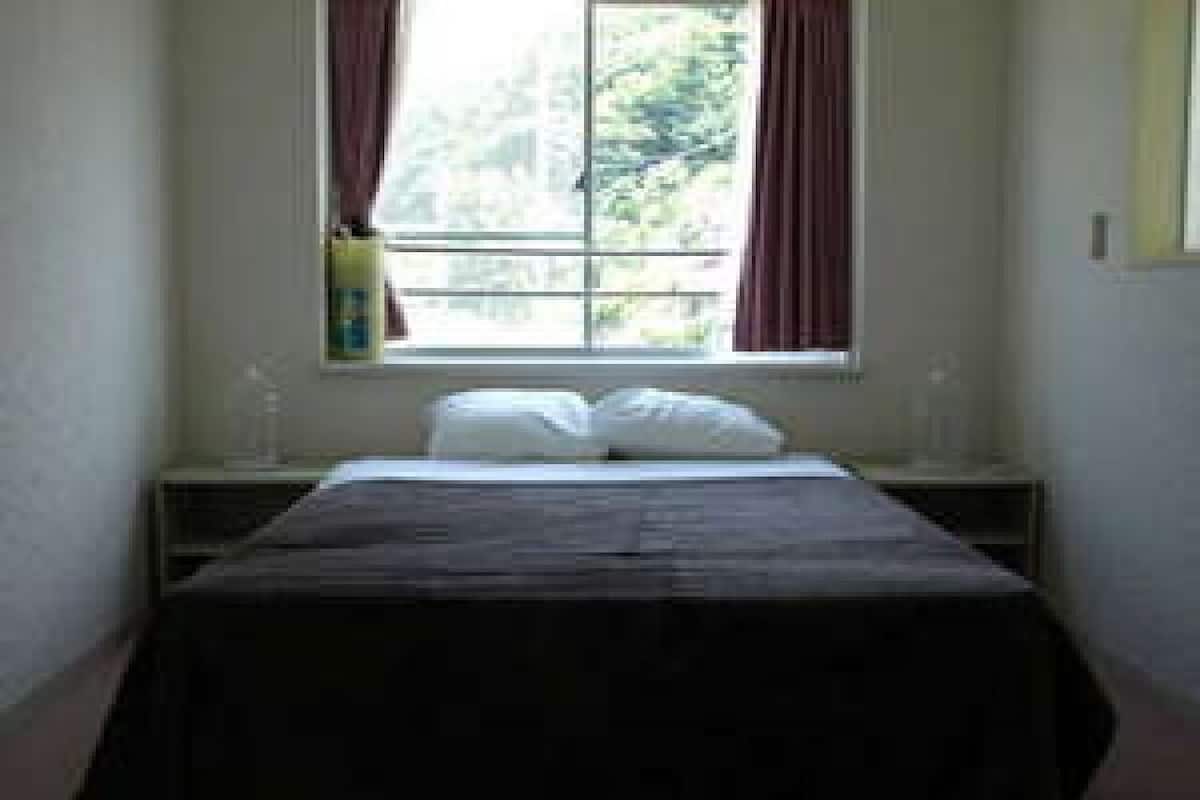 Une chambre à coucher avec un lit, une fenêtre avec des rideaux, une table de chevet et une lampe fixée au mur.