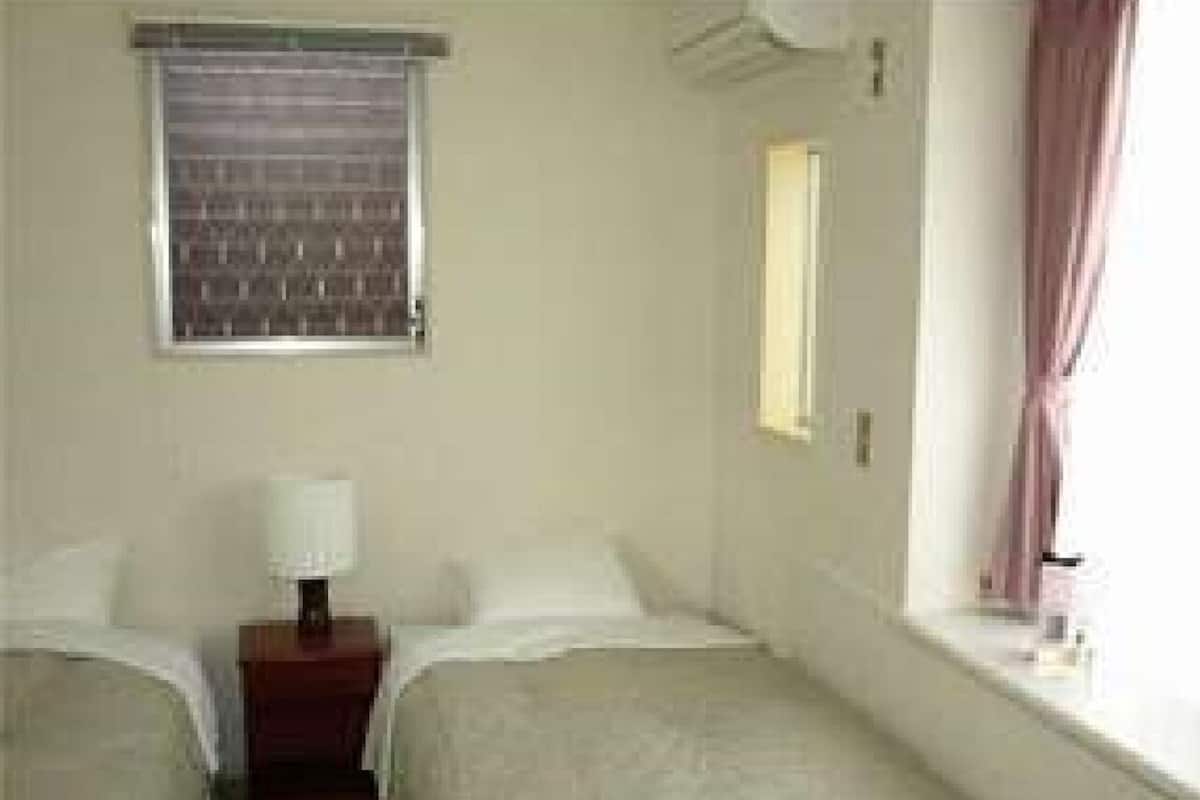 Une chambre d’hôtel avec deux lits, une table de chevet avec une lampe, une fenêtre avec des rideaux et un appareil de climatisation.