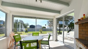 Une terrasse avec une table ronde et des chaises, une cheminée en briques et une vue sur le jardin à travers des portes vitrées.