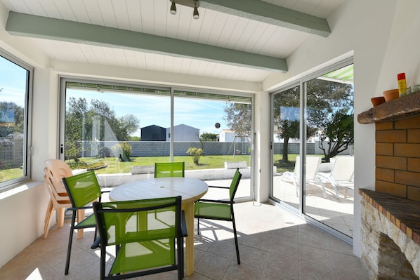 Une terrasse avec une table ronde et des chaises, une cheminée en briques et une vue sur le jardin à travers des portes vitrées.