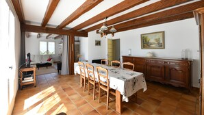 Un coin repas avec une table et des chaises en bois, un lustre et une vue sur un salon comprenant un canapé et une fenêtre.