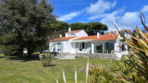 Une maison blanche avec un toit recouvert de tuiles rouges, entourée d’une pelouse bien entretenue et d’arbres.