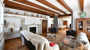 Un salon chaleureux avec une cheminée, des poutres en bois, un mur en pierre, un canapé, une table basse et une bibliothèque.