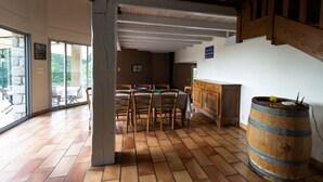 A dining area with a wooden table and chairs, a large wooden barrel, and a view of the outdoors through large windows.