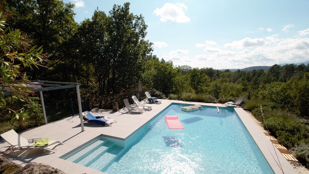 A rectangular swimming pool with clear blue water, surrounded by lounge chairs and a pergola.