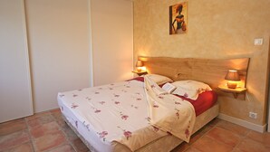 A bedroom with a wooden headboard, a bed with floral bedding, two bedside lamps, and a painting on the wall.