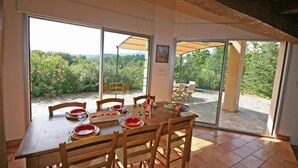 A dining area with a table set for four, chairs, and a large window offering a view of greenery and hills.