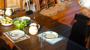 A wooden cabin with a dining table set for a meal, surrounded by a snowy landscape and a tall evergreen tree.