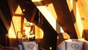 A cozy attic room with wooden beams, two upholstered chairs with heart-patterned cushions, a small table, and a patterned rug.