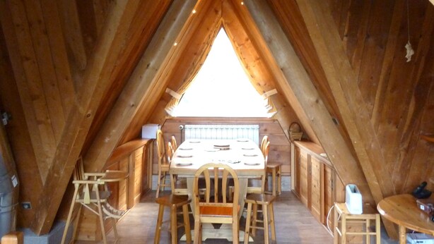 An attic room with a wooden table and chairs, a radiator, and a small stool.