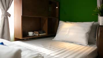 A neatly made bed with white linens, a wooden shelf with books and a cup, and a green wall in the background.