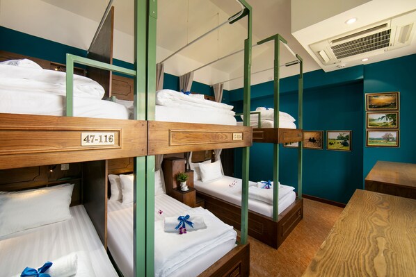 Dormitorio con literas de madera, ropa de cama blanca y una mesita pequeña.