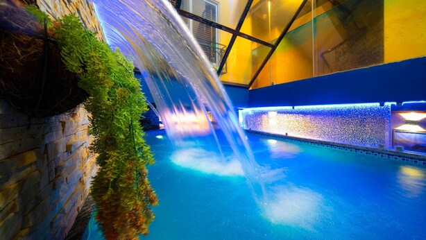 An indoor pool with a waterfall feature, surrounded by stone walls and glass panels. - Little Charm Hanoi Hostel (Hanoi)